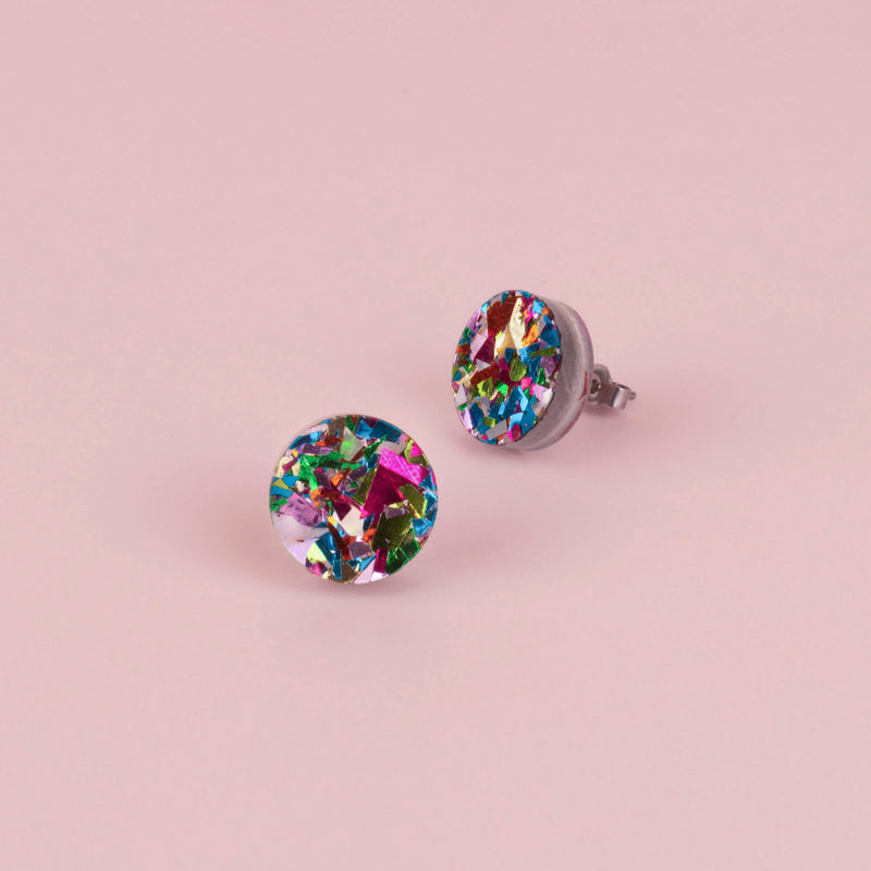 Pair of round rainbow confetti glitter stud earrings in pink, green, blue and gold flecks, on pale pink paper