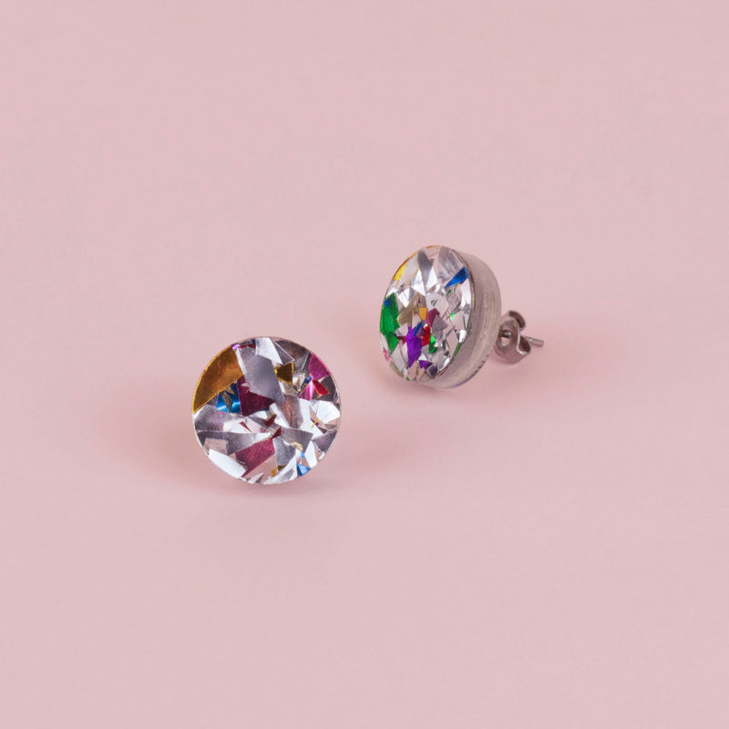 Pair of round silver confetti glitter stud earrings with gold, green and pink flecks, on pale pink paper