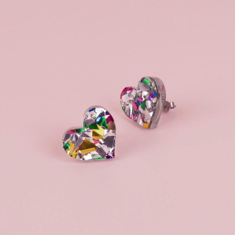 Pair of silver confetti glitter heart stud earrings with gold, green and pink flecks, on pale pink paper