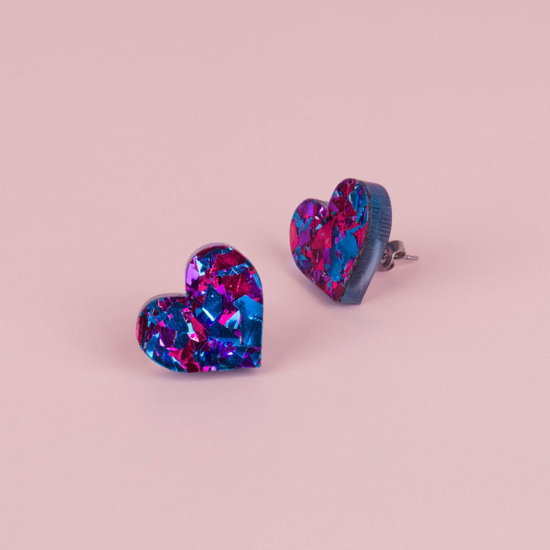 Pair of purple and blue confetti glitter heart stud earrings with magenta flecks, on pale pink paper