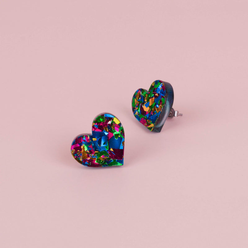 Pair of green and blue confetti glitter heart stud earrings with pink and gold flecks, on pale pink paper