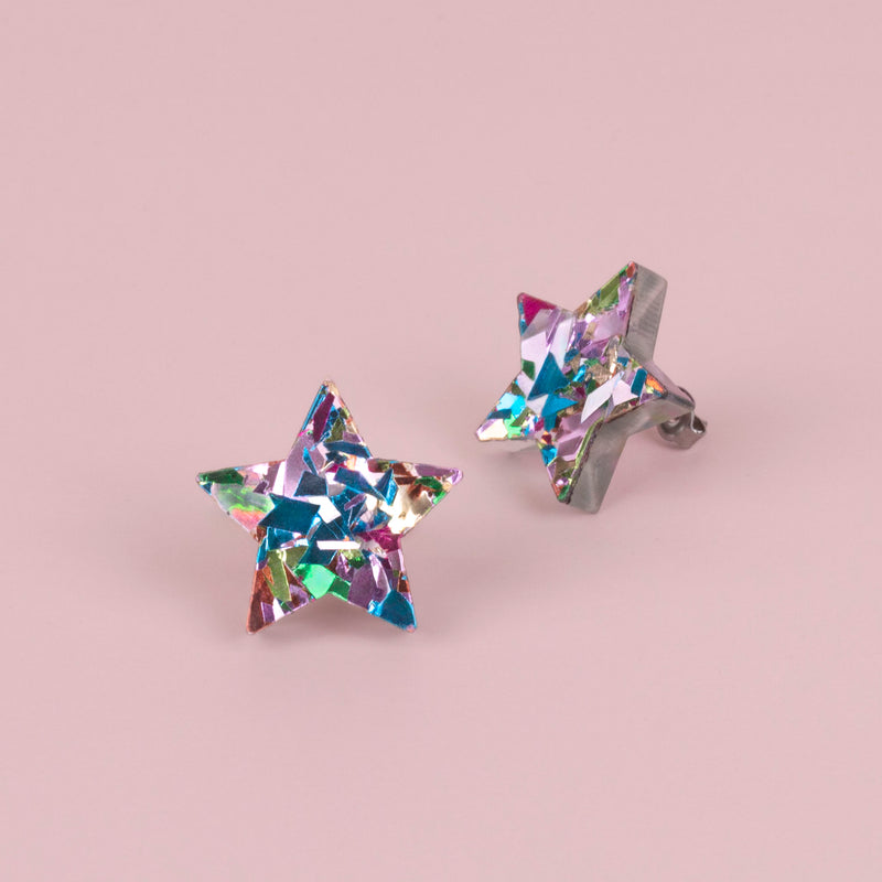 Pair of rainbow confetti star studs in pink, teal and lilac holographic glitter on pink paper, one seen from the side