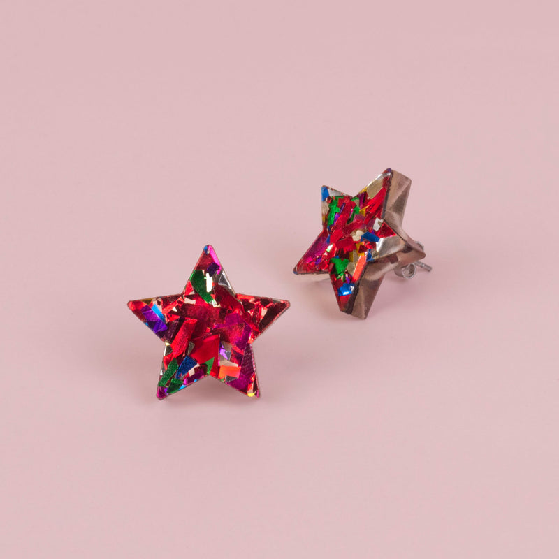 Pair of red confetti glitter star studs on pink paper, one shown front on and one from the side with its post