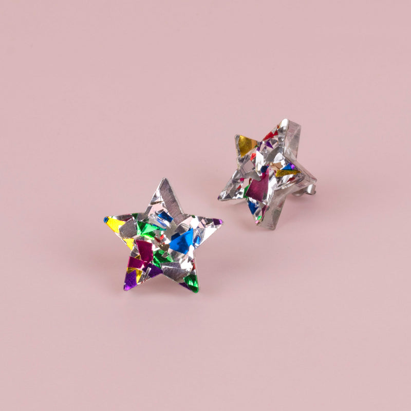 Pair of silver confetti glitter star studs with rainbow flecks on pink paper, one front on and one side on