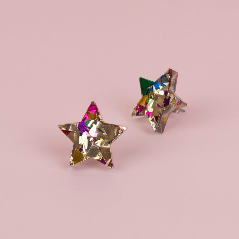 Pair of gold confetti glitter star stud earrings with pink, purple and green flecks, on pale pink paper