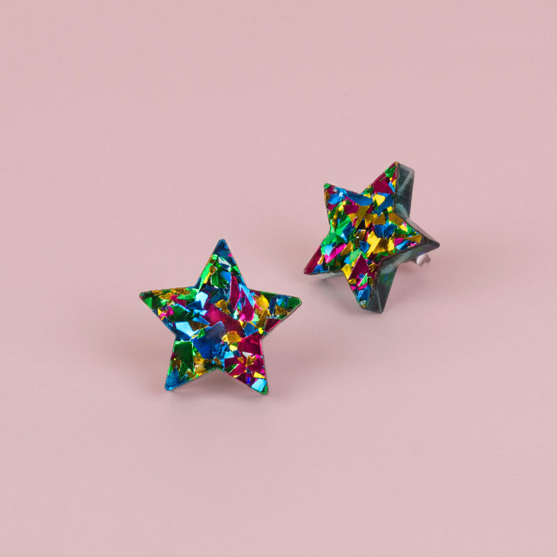 Pair of green confetti glitter star stud earrings with blue, gold and pink flecks, on pale pink paper
