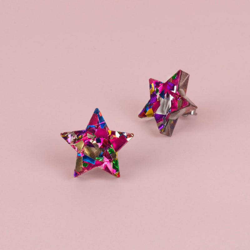 Pair of pink confetti glitter star stud earrings with blue, gold and green flecks, on pale pink paper