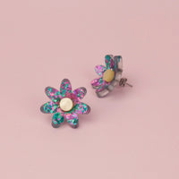 Lilac and turquoise confetti flower studs with pale gold centres on pink paper, one tilted to show the back