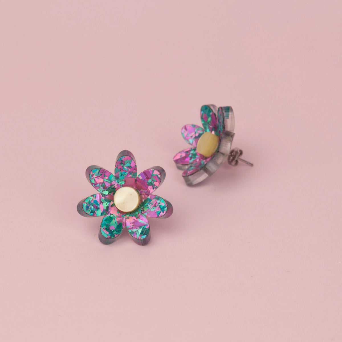 Lilac and turquoise confetti flower studs with pale gold centres on pink paper, one tilted to show the back