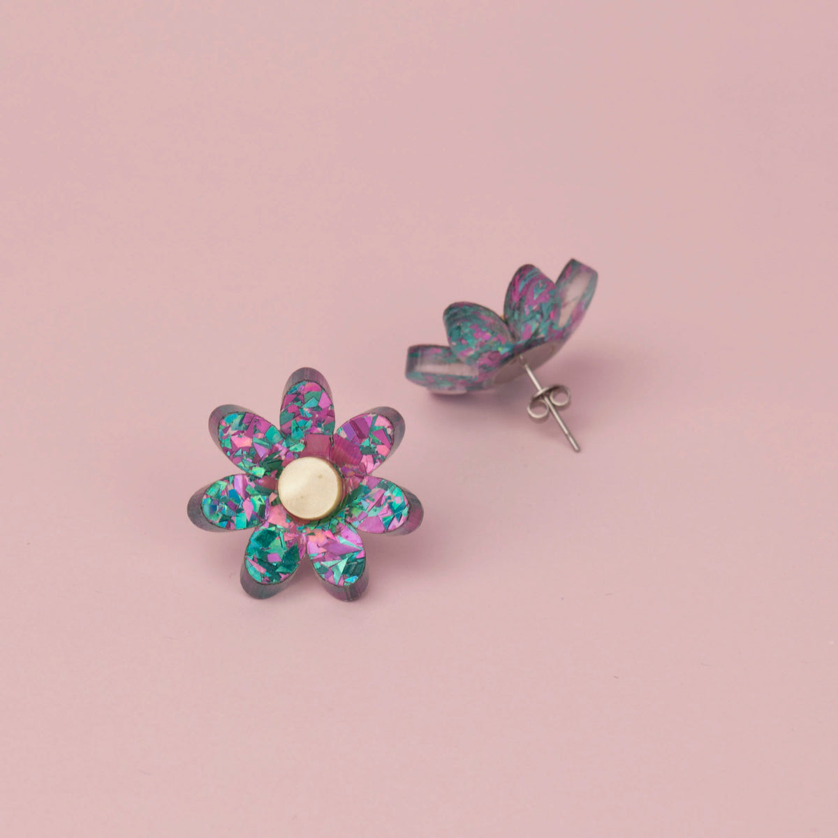 Lilac and turquoise flower stud face up with its pair showing the silver post and butterfly back, on pink