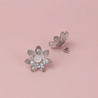 Silver holographic flower stud face up beside its pair showing the post and butterfly back, on pink paper