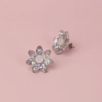 Silver holographic confetti flower studs with white pearly centres on pink paper, one tilted to show its back