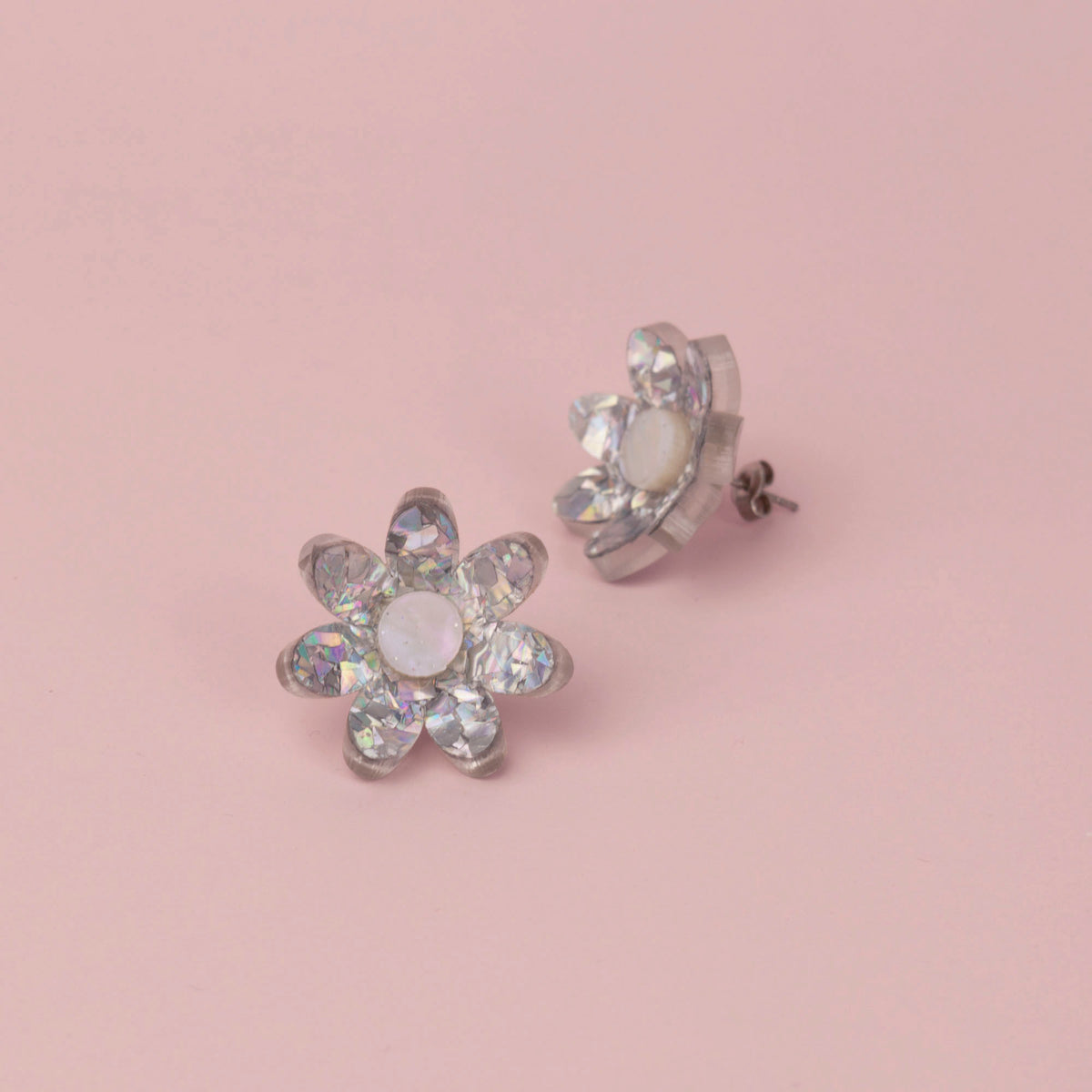 Silver holographic confetti flower studs with white pearly centres on pink paper, one tilted to show its back