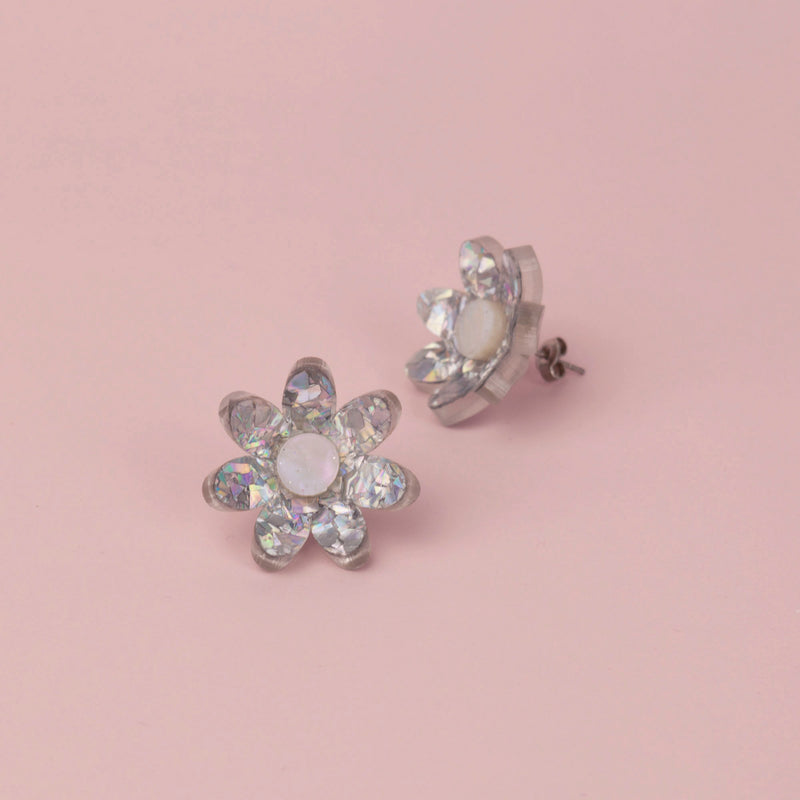 Silver holographic confetti flower studs with white pearly centres on pink paper, one tilted to show its back