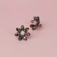 Rainbow confetti flower studs with multicoloured glitter petals and white centres on pink, one tilted to show the post
