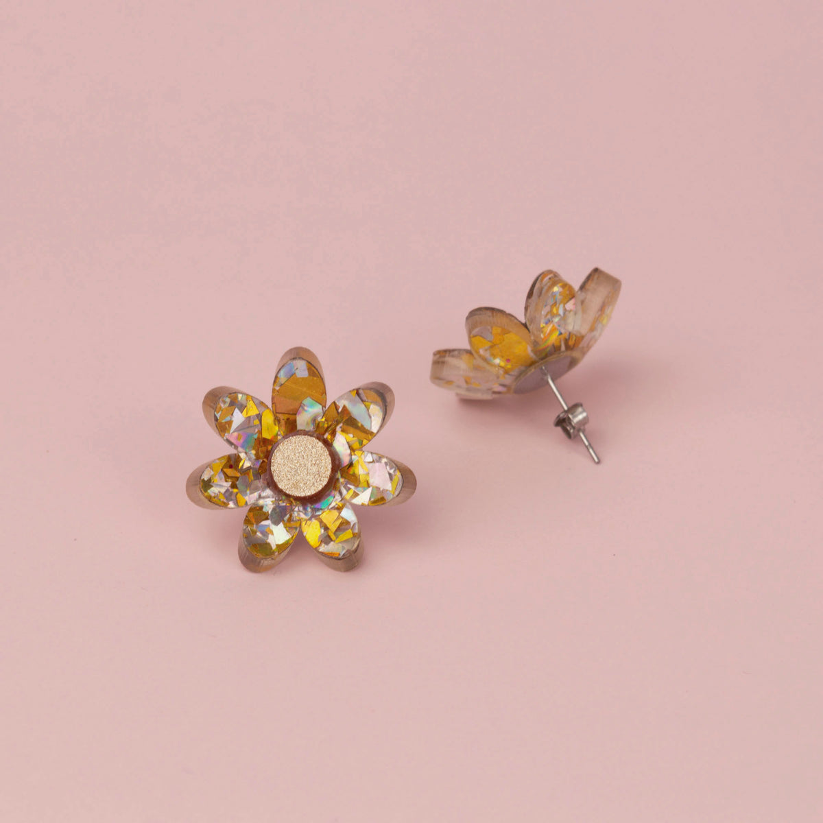 Silver and gold flower stud face up beside its pair standing on its silver post, on pink paper