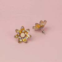 Silver and gold flower stud face up beside its pair standing on its silver post, on pink paper