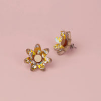 Silver and gold holographic confetti flower studs with gold glitter centres on pink paper, one tilted on its side