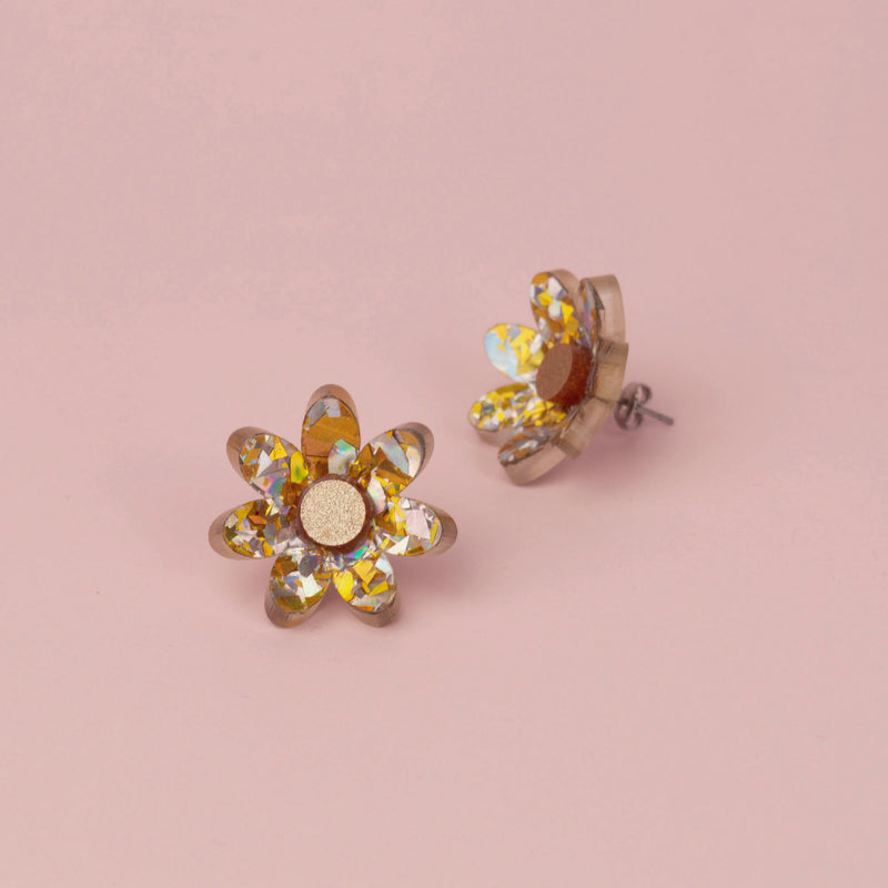 Silver and gold holographic confetti flower studs with gold glitter centres on pink paper, one tilted on its side