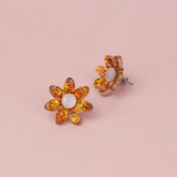 Pair of orange holographic confetti flower studs on pink paper with white pearl centres, one showing the post
