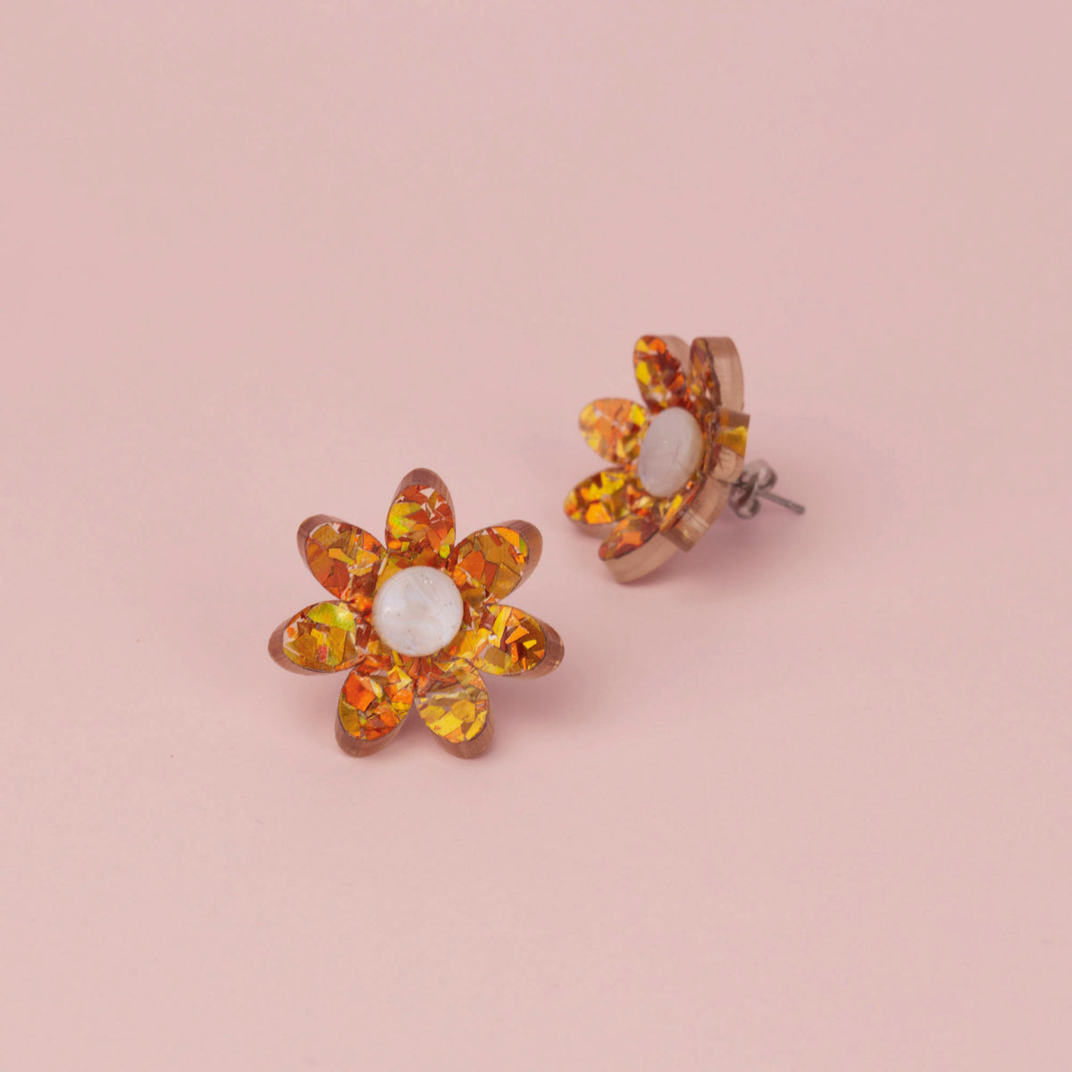 Pair of orange holographic confetti flower studs on pink paper with white pearl centres, one showing the post