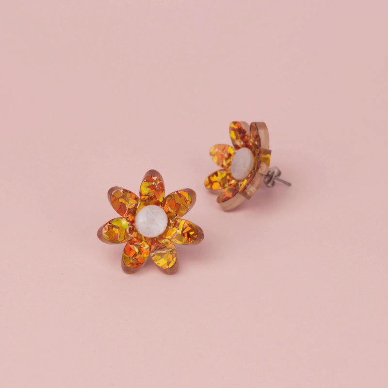 Pair of orange holographic confetti flower studs on pink paper with white pearl centres, one showing the post