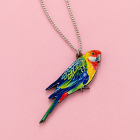Rosella parrot pendant with red head, yellow chest and blue-green wings, on a silver curb chain over pink paper