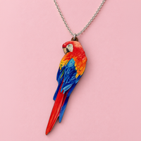 Red macaw pendant with red, orange and blue painted feathers and a long tail, on a silver chain over pink paper