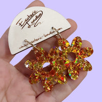 Orange and gold confetti flower earrings with gold hoops held in a hand against their wooden display card