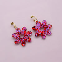 Pink and red confetti flower dangle hoop earrings with gold hoops, laid flat on pale pink paper