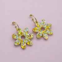 Gold and silver holographic confetti flower dangle hoops with gold hoops, laid flat on pale pink paper