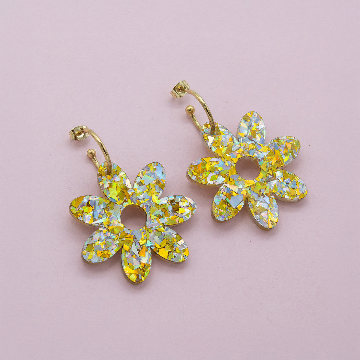 Gold and silver holographic confetti flower dangle hoops with gold hoops, laid flat on pale pink paper