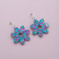 Lilac and turquoise confetti flower dangle hoop earrings with silver hoops, laid flat on pale pink paper