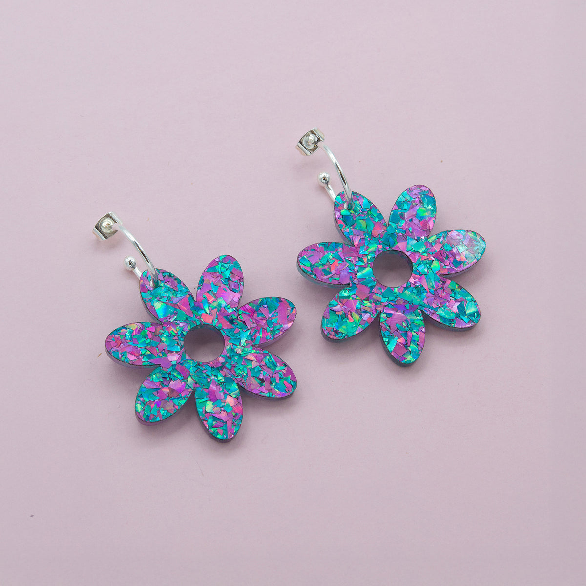 Lilac and turquoise confetti flower dangle hoop earrings with silver hoops, laid flat on pale pink paper
