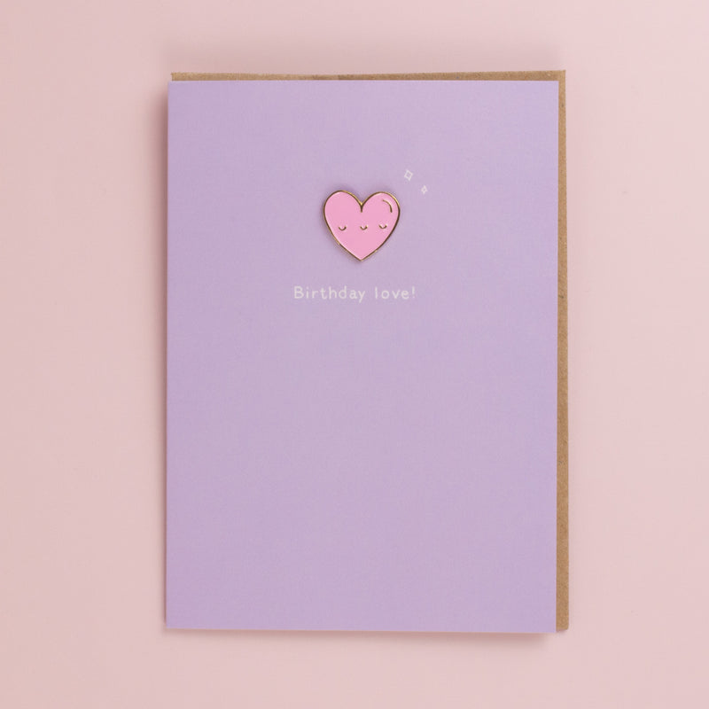 Lilac birthday card with a pink enamel heart pin with a sleepy face, small sparkles and white text, kraft envelope behind