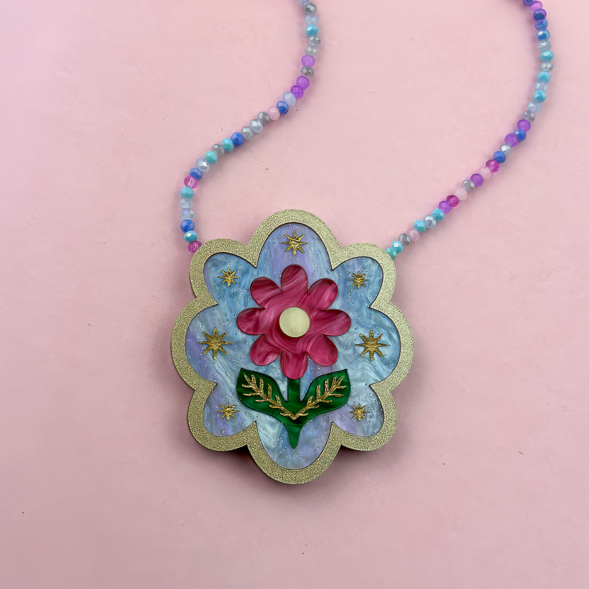 Scalloped necklace with a pink flower, green leaves and gold stars on blue acrylic, gold glitter edge, pastel bead chain